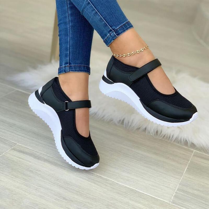 Black mesh strap sneakers on a white sole, worn with skinny jeans, side view