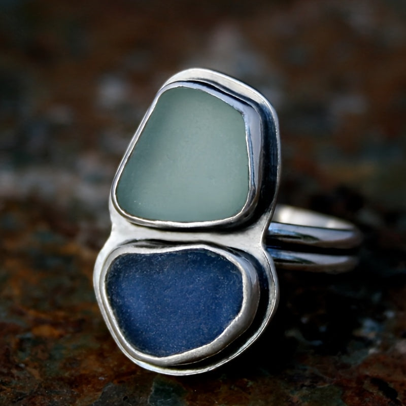 Ring with two smooth stones, one pale and one deep blue, set in polished metal bezels on a split band