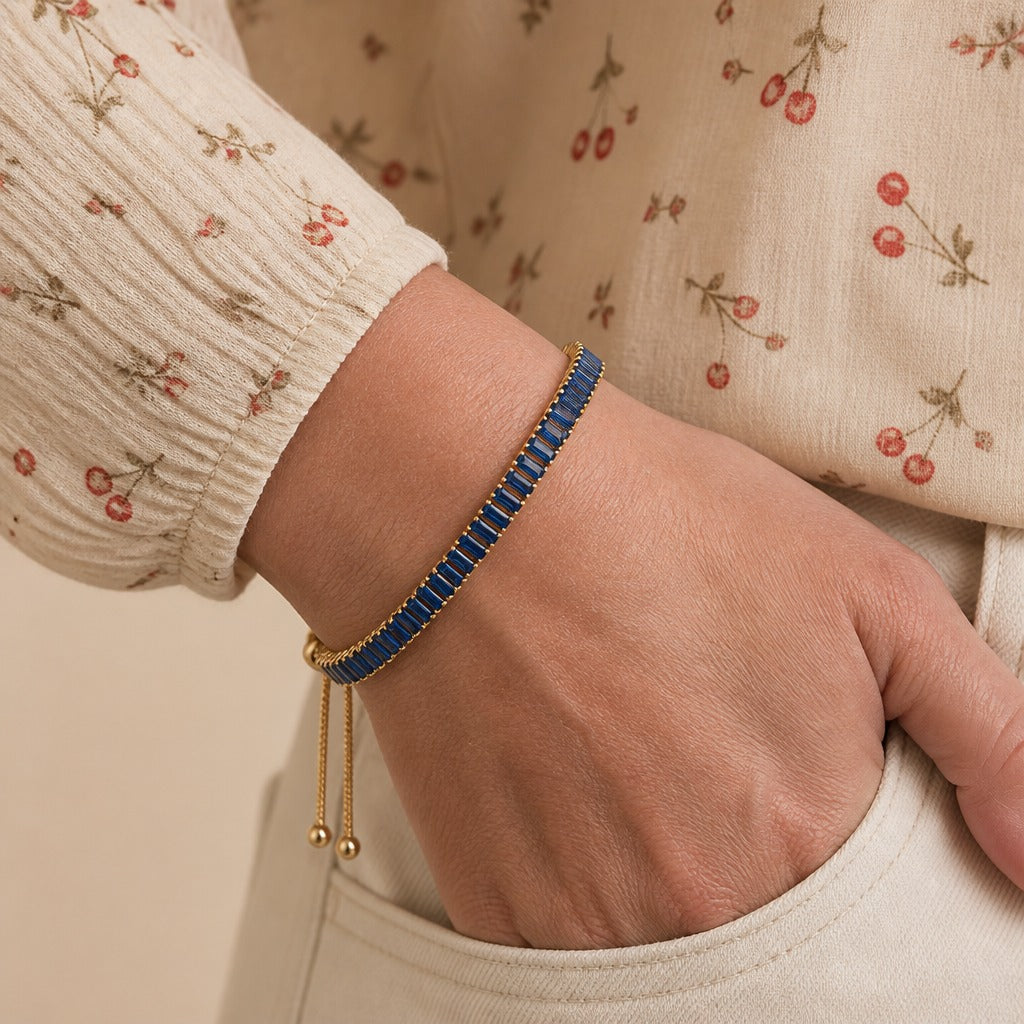 Wrist wearing a blue baguette crystal tennis bracelet with ball-end slider chains, hand in a pocket