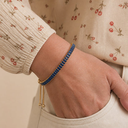 Wrist wearing a blue baguette crystal tennis bracelet with ball-end slider chains, hand in a pocket