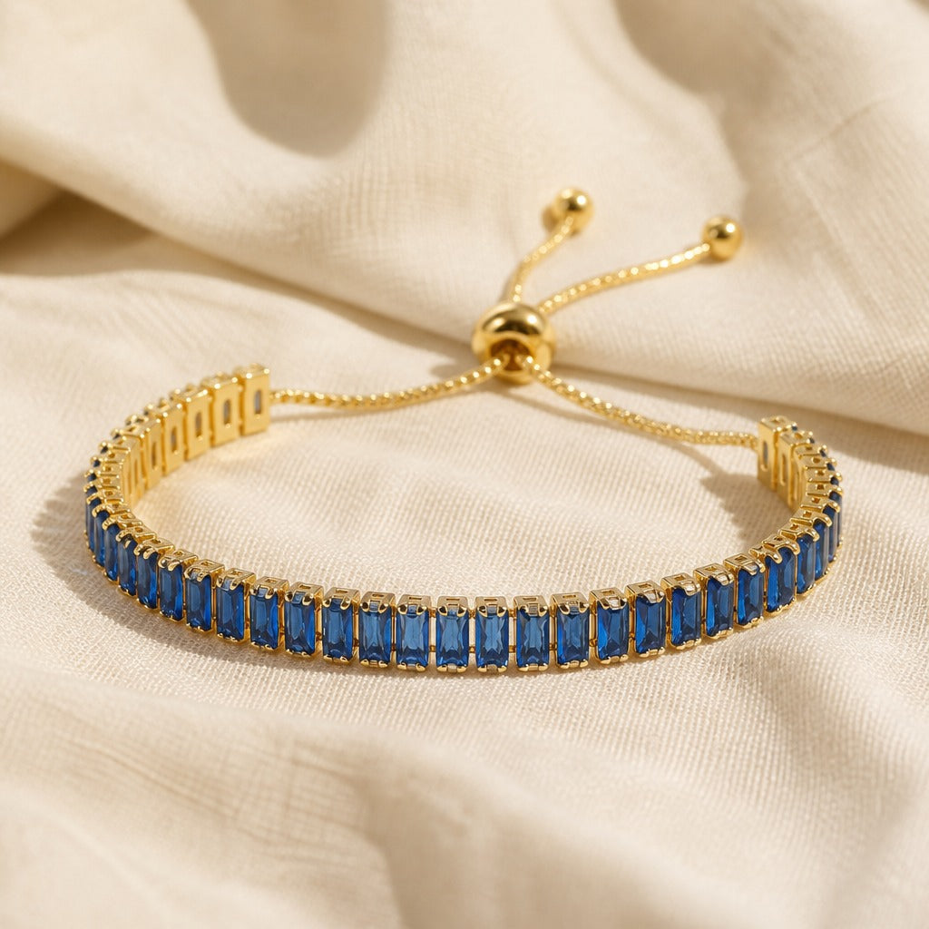 Blue baguette crystal tennis bracelet with gold ball-end slider chains on a cream fabric
