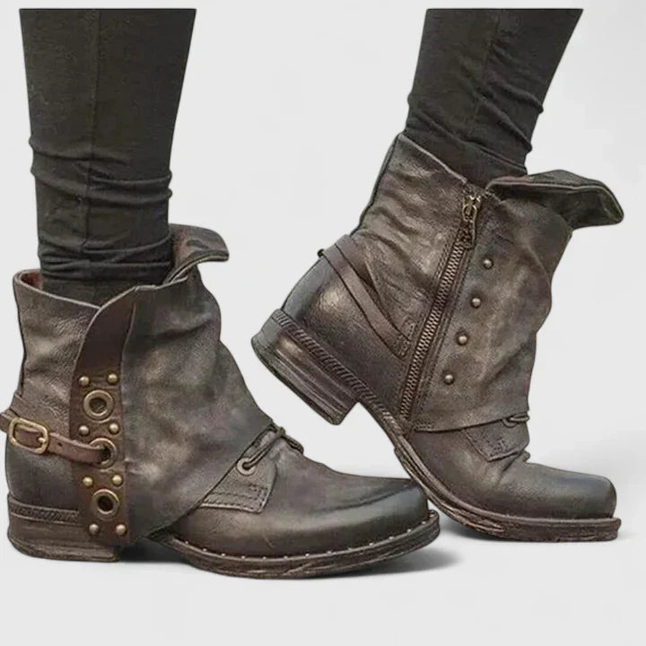 Brown ankle boots with buckled strap, grommet panel and studs, worn with black leggings