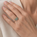 Hand wearing a small butterfly ring with glossy teardrop stones in its wings, on a cream fabric