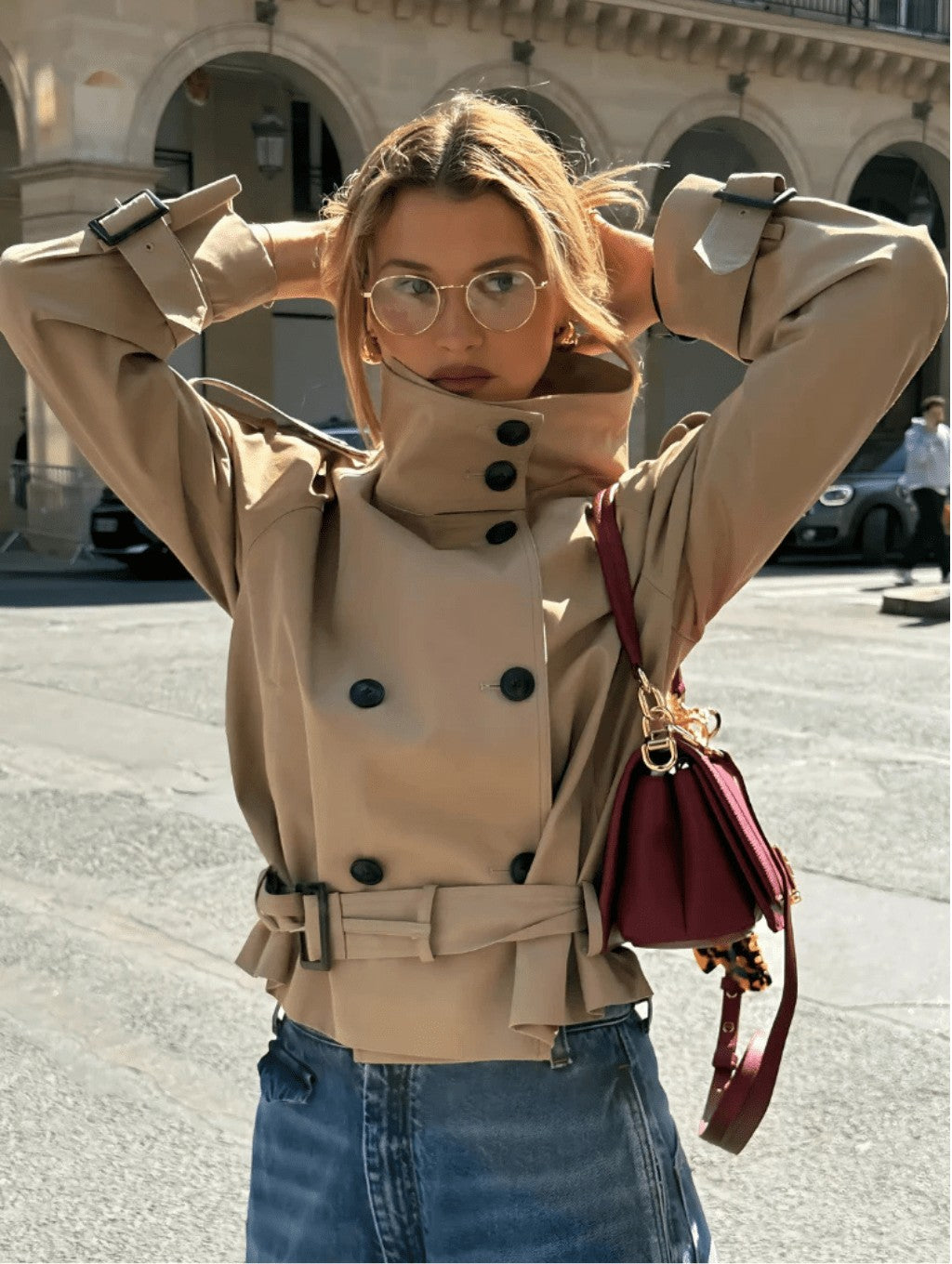 Woman in a beige cropped trench jacket with funnel collar and belt on a city street