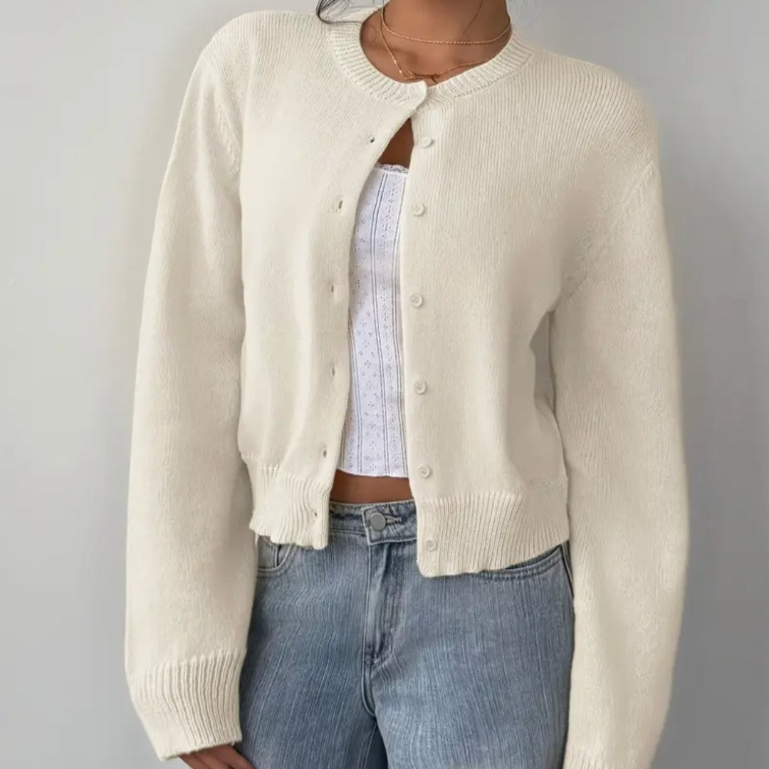 Woman wearing a white cropped crew neck cardigan over a camisole with light jeans, front view