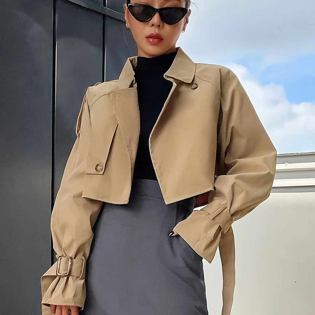 Woman in a khaki cropped trench jacket with buckled cuff straps over a gray pencil skirt, front view