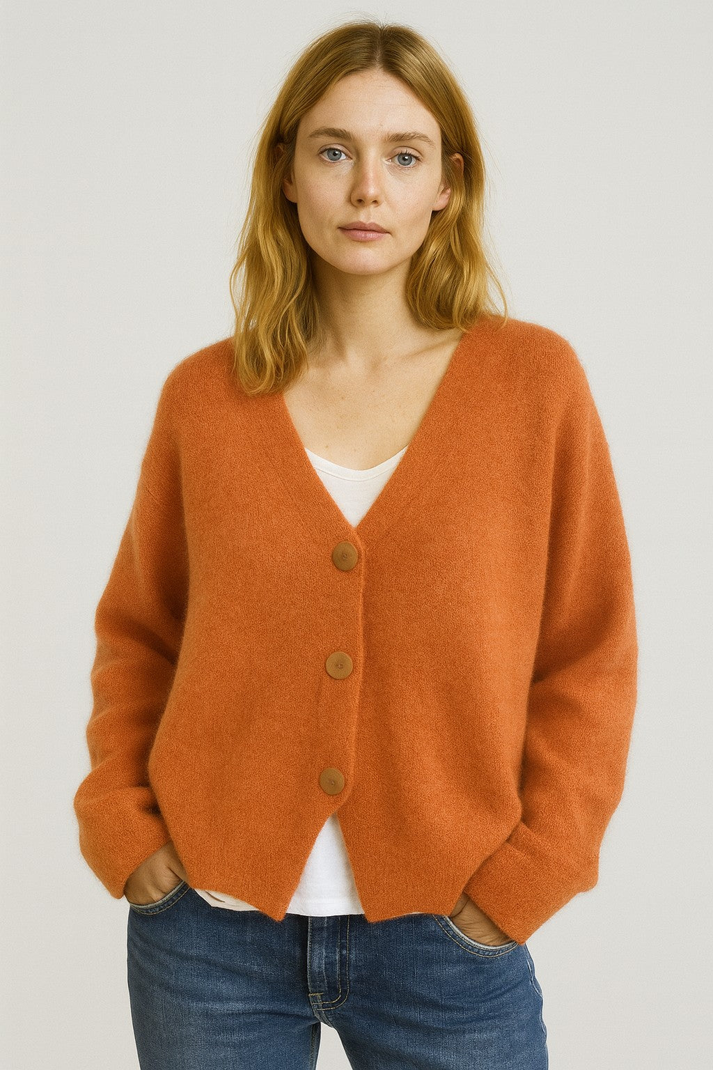 Woman wearing an orange cropped V-neck cardigan over a white tee with blue jeans, front view