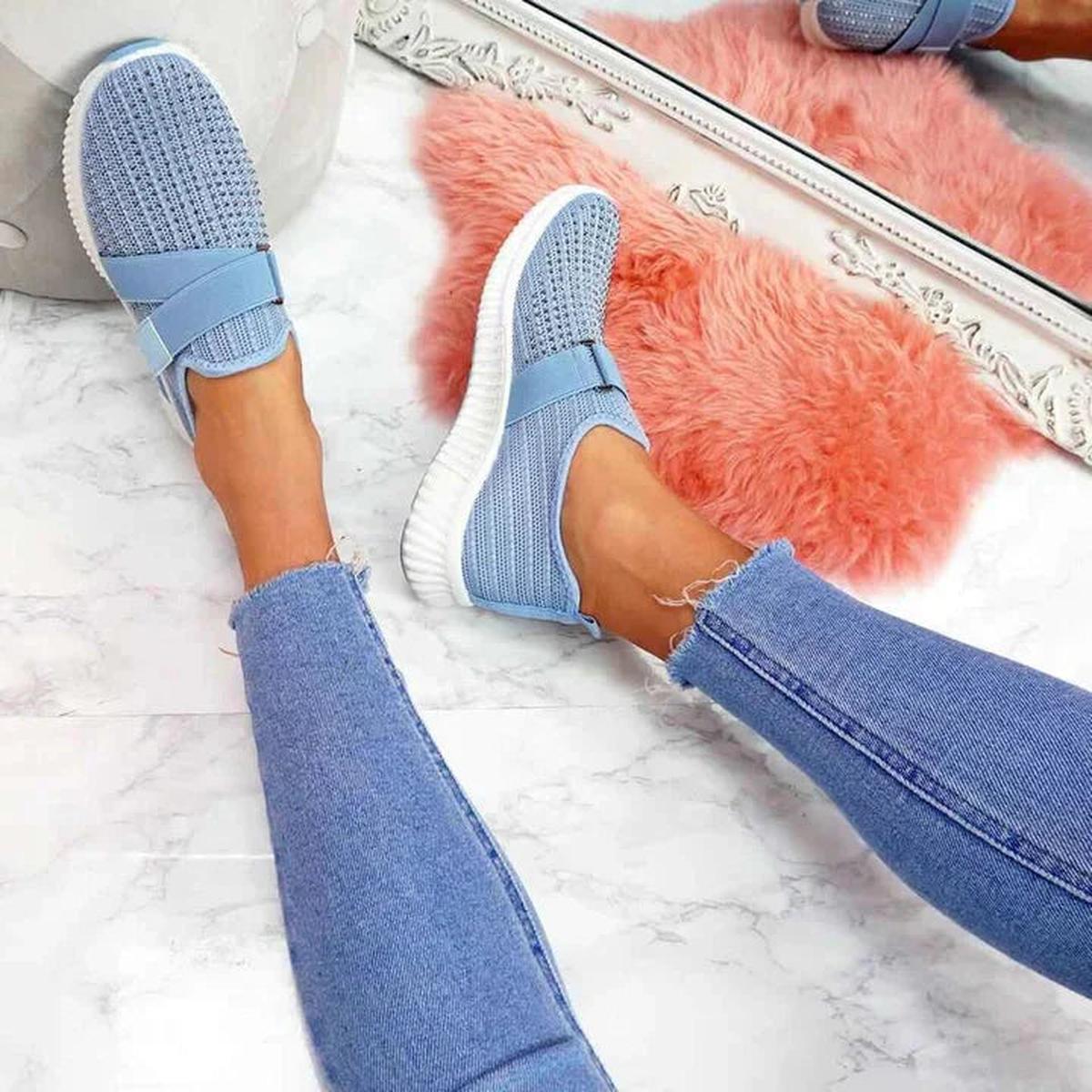 Blue elastic strap sneakers worn with skinny jeans, top view on a marble floor