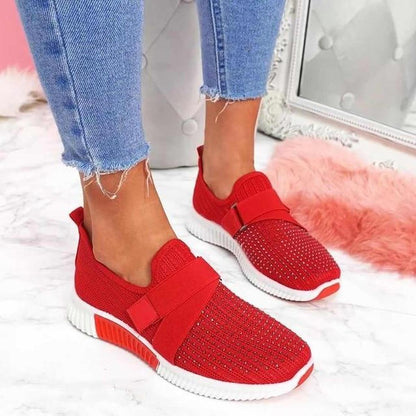 Red elastic strap sneakers with a studded toe and white sole, worn with cropped jeans