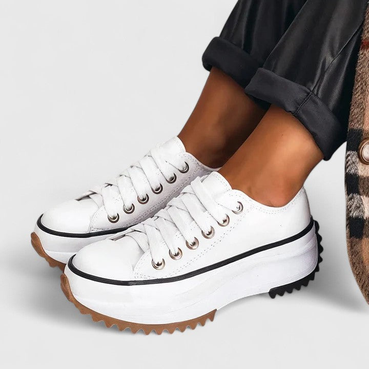 White low top platform sneakers with lug sole worn with rolled black pants