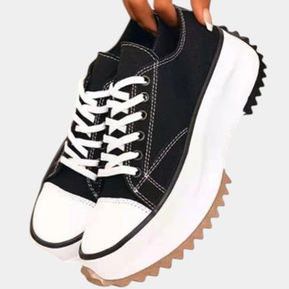 Black low top platform sneakers with white toe cap held in hand