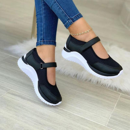 Black mesh strap sneakers on a white sole, worn with skinny jeans, side view