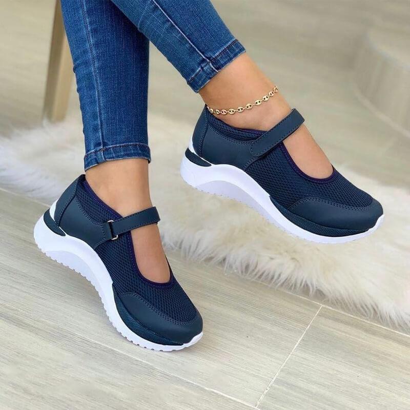 Navy blue mesh strap sneakers on a white sole, worn with skinny jeans, side view