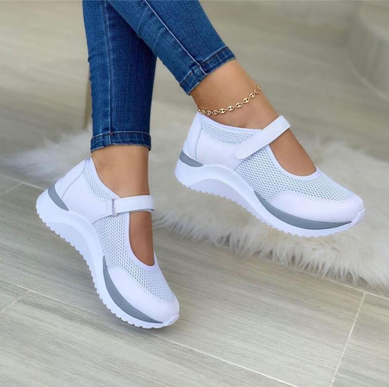 White mesh strap sneakers with a gray sole stripe, worn with skinny jeans, side view
