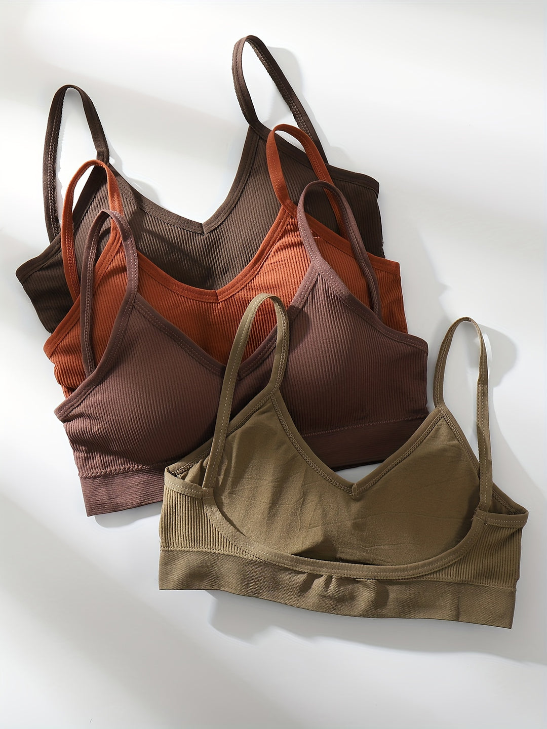 Four ribbed bralettes in olive, mauve, rust and coffee laid flat with thin straps and V necklines