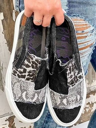 Black patchwork slip-on sneakers held in hand, top view of the print panels