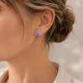 Close-up of a woman's ear wearing a small raw-cut purple amethyst stud earring with her hair in an updo