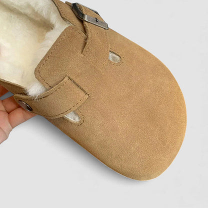 Close up of a tan suede clog with cream shearling lining and a metal buckle strap