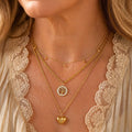 Woman wearing a layered necklace with a tree of life disc and a heart pendant on three chains