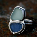 Ring with two smooth stones, one pale and one deep blue, set in polished metal bezels on a split band