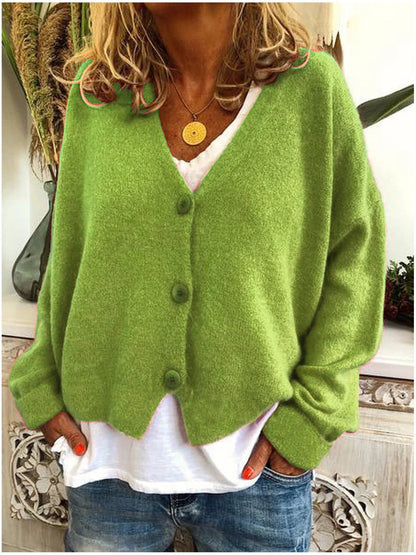 Green V neck button front cardigan worn open over a white top and jeans