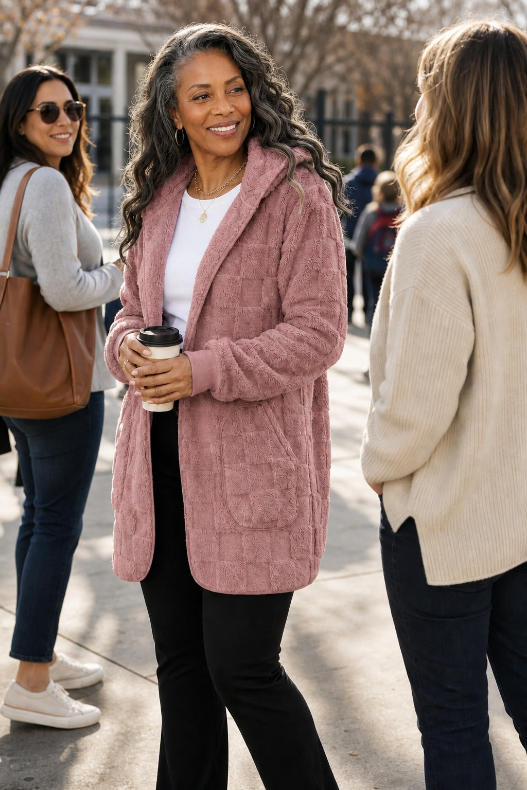 Three women walking, one in a dusty pink plush hooded cardigan