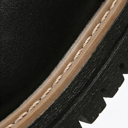 Close-up of a black ankle boot showing the contrast stitched welt and lugged platform sole