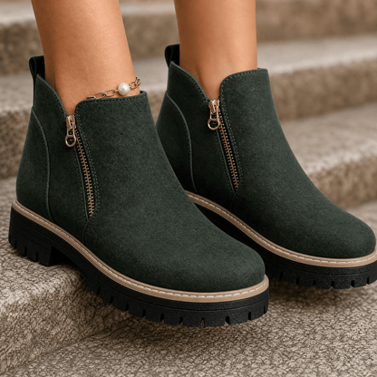 Dark green suede platform ankle boots with gold side zips and lug soles, worn on stone steps