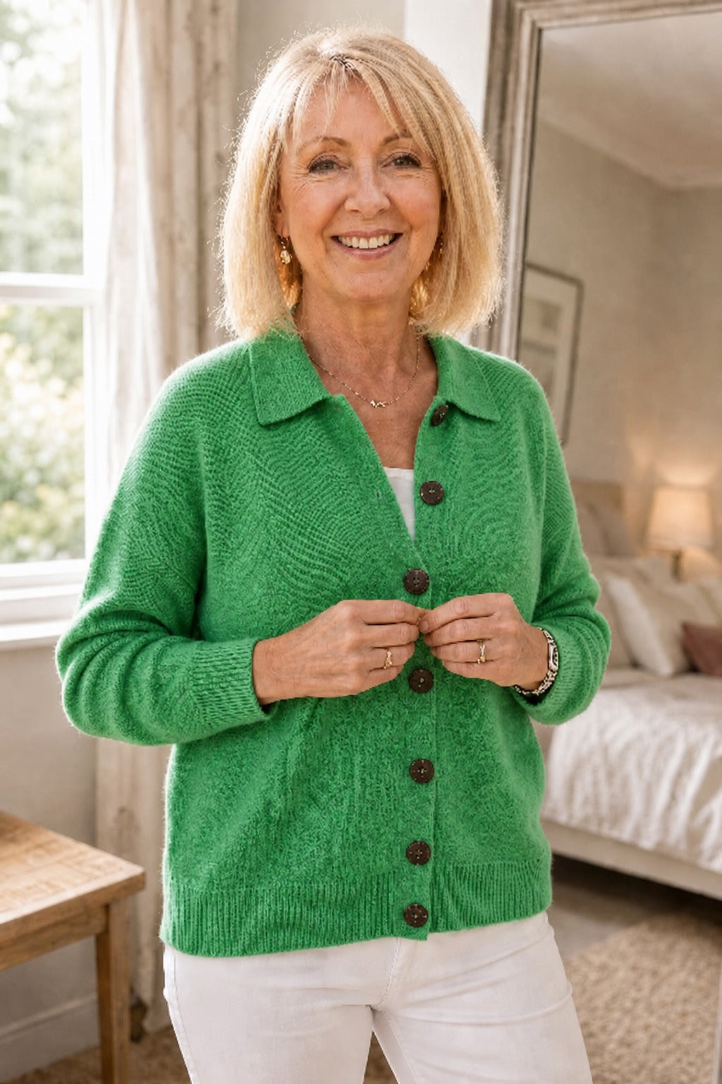 Woman in a bedroom buttoning a green knit collared cardigan