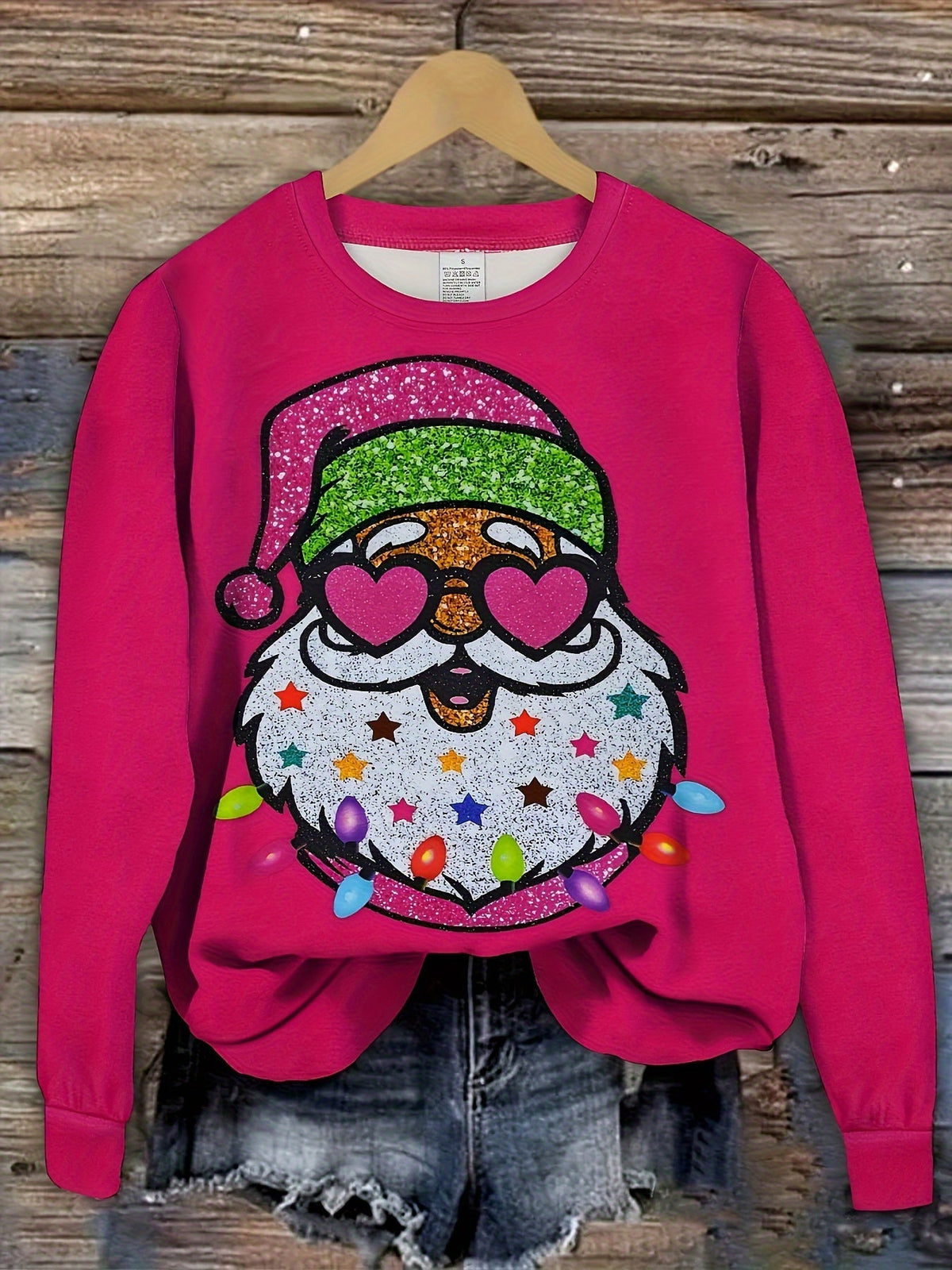 Hot pink Santa graphic sweatshirt on a hanger against rustic wood