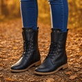 Pair of black lace up boots with studded cuffs, worn with jeans on autumn leaves